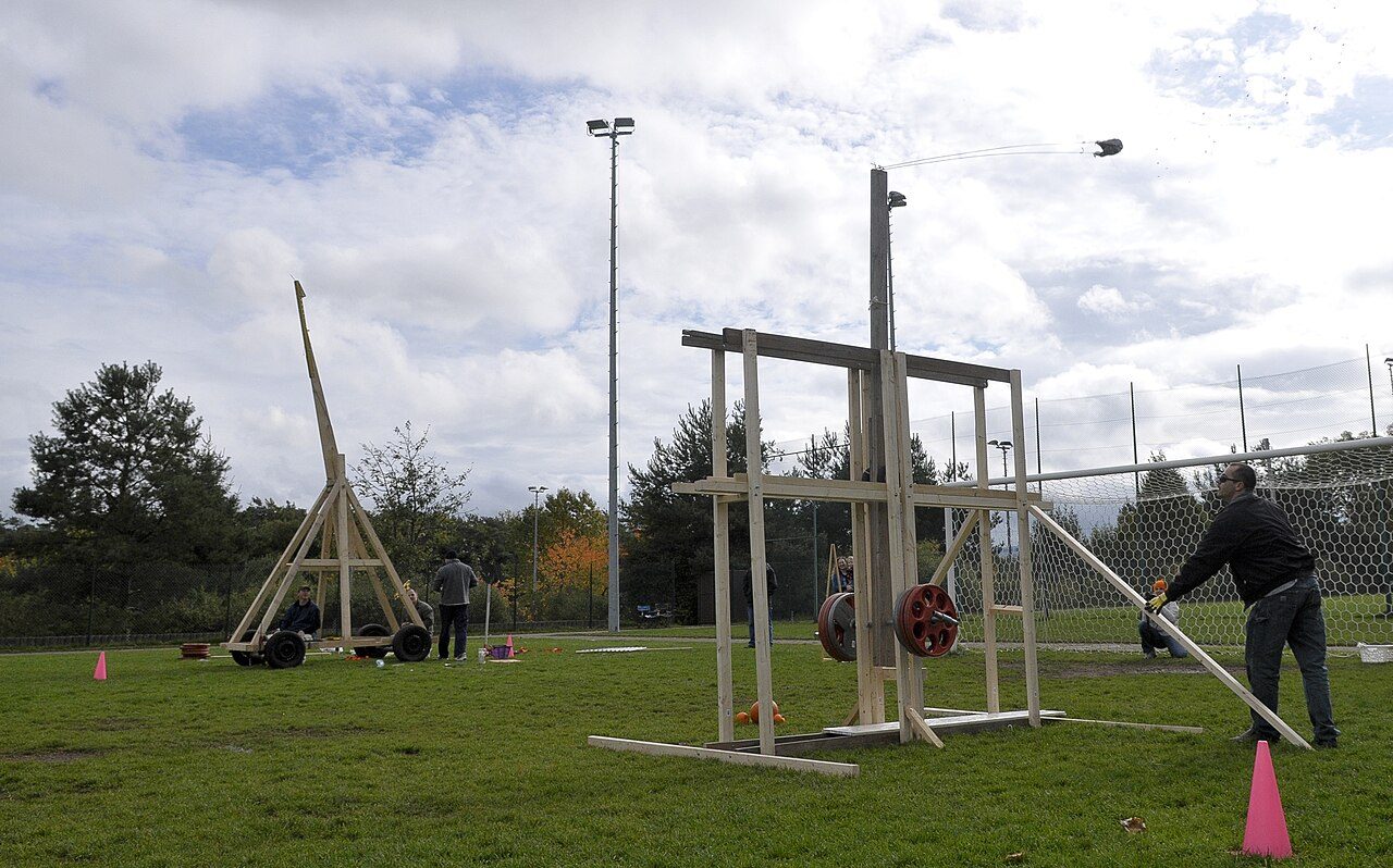 Tall timber trebuchets throwing pumpkins across a field at a pumpkin-throwing contest